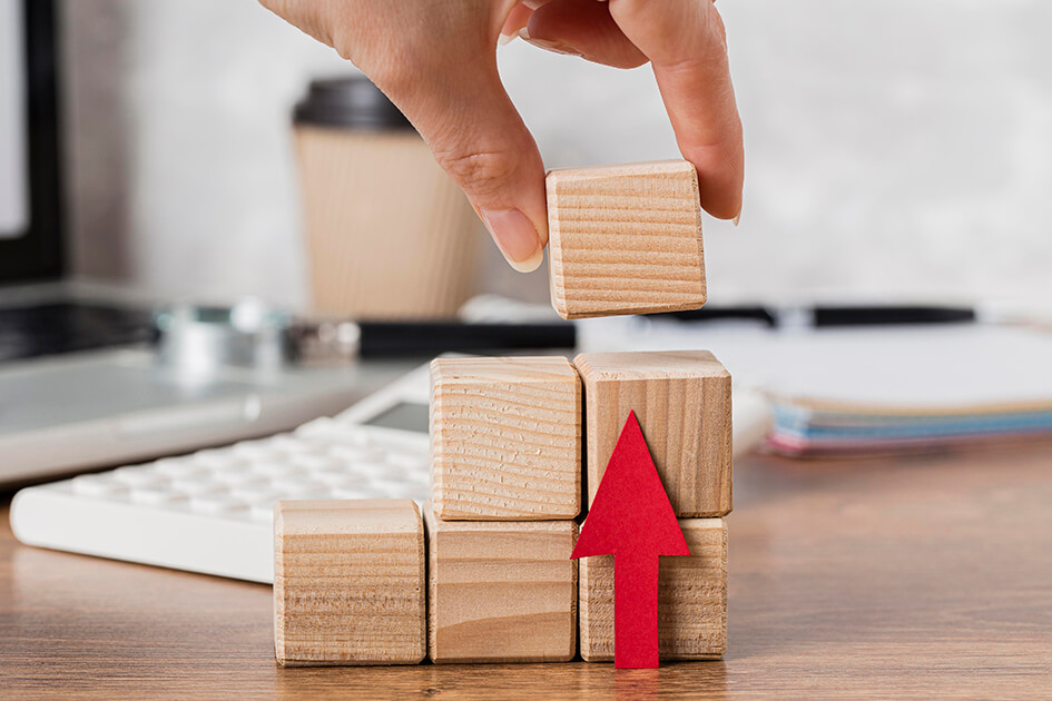 Hand stacking of six wooden cubes with a red arrow pointing up representing growth